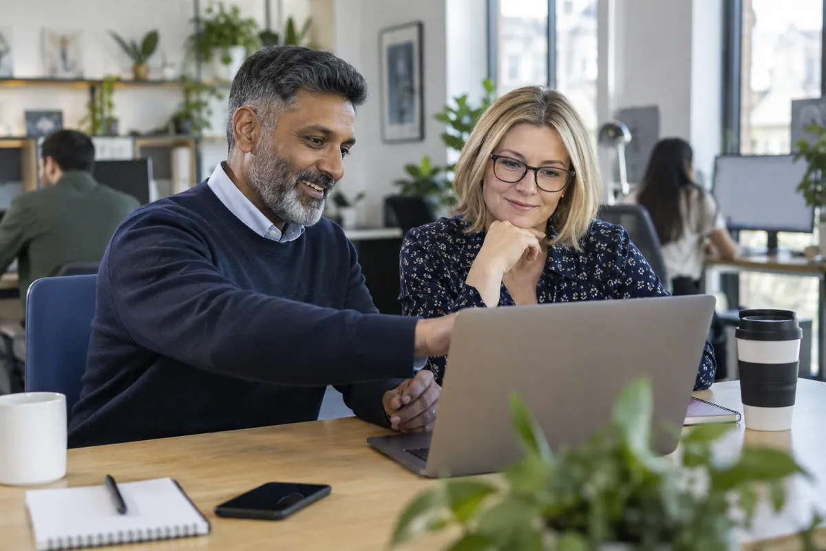Two colleagues reviewing a laptop together in a bright shared office